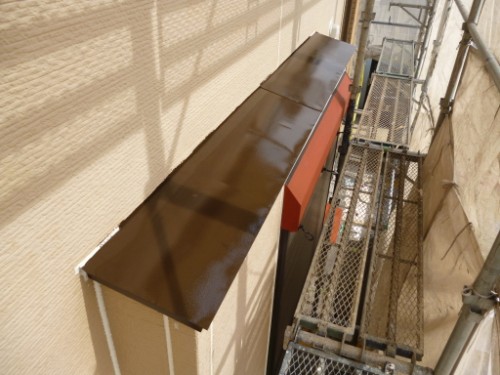 Brown metal awning projecting from a beige building over a doorway, with construction scaffolding visible along the wall nearby.