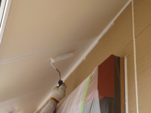 Painter in a glove rolls white paint onto the ceiling with a roller; doorway is covered in plastic sheeting and taped for protection.