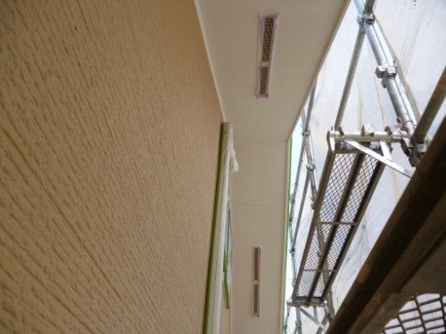 Narrow construction corridor with beige walls, ceiling lights, and metal scaffolding on the right side.