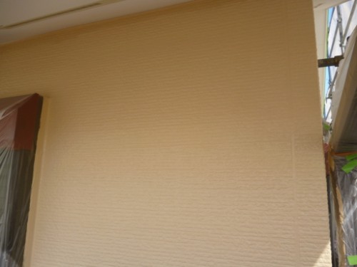 Beige textured exterior wall of a building under renovation, with scaffolding and plastic sheeting visible on the right.