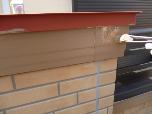 Close-up of beige paint being applied with a roller along a brick pillar, with a red coping edge above.