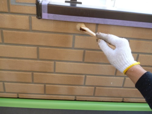 Gloved hand using a wooden tool to patch a brick wall beneath a window.