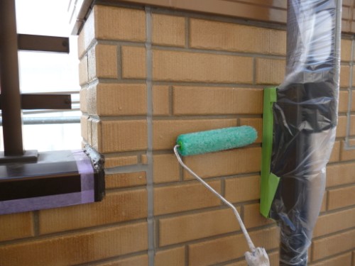 Green paint roller applying paint to a brick wall near a balcony railing.