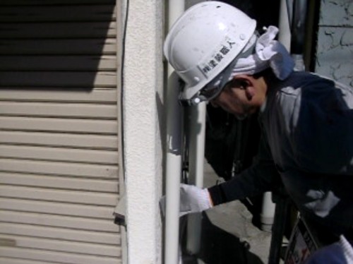 shitaji_chousei | 外壁塗装は神奈川県横浜市の塗装職人 Construction worker in a white hard hat and gloves inspecting a doorway on a building exterior.