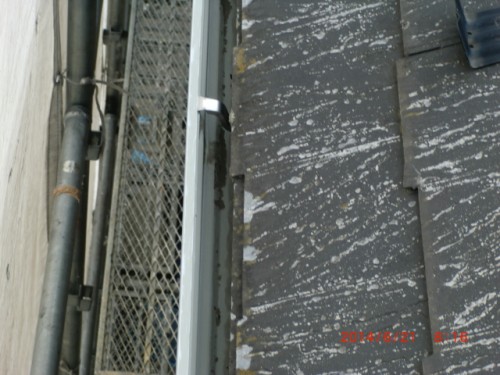 Close-up of a sloped roof with black weathered shingles and metal flashing, next to scaffolding on a construction site.