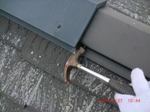 A gloved hand holds a claw hammer against metal roof flashing, tapping or prying at the seam.