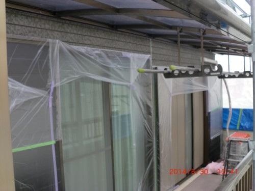 Building exterior under renovation; plastic sheeting covers the windows, scaffolding overhead, and a metal rod with hooks is mounted to the wall.