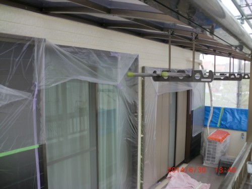 Balcony under renovation with plastic sheeting over sliding doors, scaffolding rails, and construction materials covered for protection