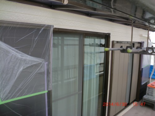 Exterior view of a building under construction with plastic sheeting covering a sliding door and window, and a metal support arm with green end caps extending from a balcony.