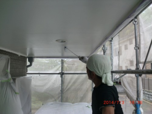 Worker wearing a head wrap paints the underside of a white ceiling with a roller inside scaffolding.