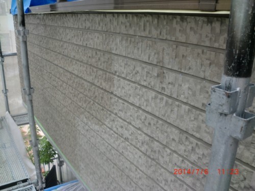 Exterior building wall with textured horizontal siding under construction, flanked by scaffolding and metal supports.