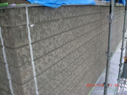Close-up of a textured concrete block wall under construction with scaffolding and a blue tarp on top.