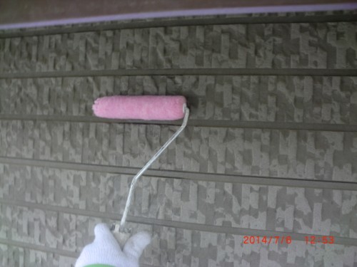 Person wearing a white glove rolls pink paint onto a gray textured exterior wall using a paint roller.