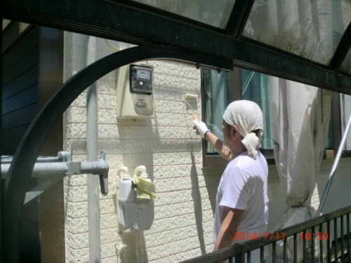 Maintenance worker in a white shirt and head covering points at an outdoor utility meter mounted on a building exterior.