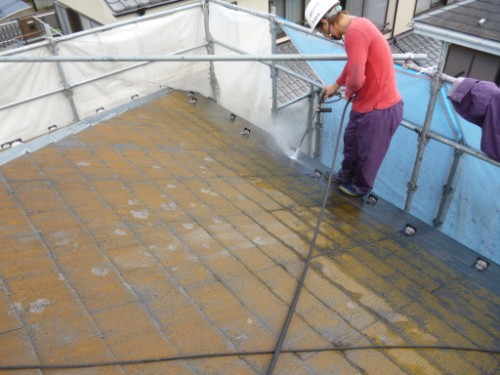 koushin_P1050763-1 | 外壁塗装は神奈川県横浜市の塗装職人 Worker wearing a hard hat sprays a protective coating on a flat roof, surrounded by scaffolding and blue tarps.