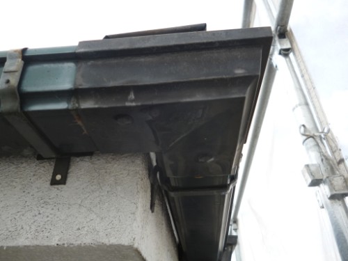 koushin_P1050777-1 | 外壁塗装は神奈川県横浜市の塗装職人 Close-up of a black metal gutter along a concrete wall with scaffolding on the right side.