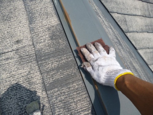 koushin_P1050829-1 | 外壁塗装は神奈川県横浜市の塗装職人 Gloved hand scrubbing a metal roof seam with a brown abrasive pad on a dark roof surface.