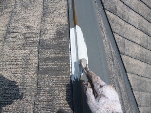 koushin_P1050830-1 | 外壁塗装は神奈川県横浜市の塗装職人 Close-up of a gloved hand painting white sealant along a metal roof flashing with a small brush.