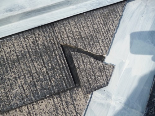 koushin_P1050839-1 | 外壁塗装は神奈川県横浜市の塗装職人 Cracked asphalt shingles on a roof with a gap exposing the underlayment beside white roof flashing, indicating potential leak risk
