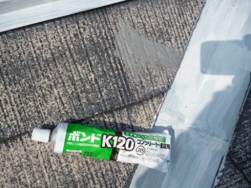 koushin_P1050840-1 | 外壁塗装は神奈川県横浜市の塗装職人 Tube of Bond K120 construction adhesive lying on a roof with a bead of white sealant nearby, on gray shingles.