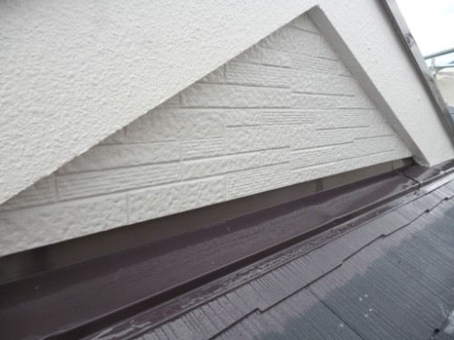 koushin_P1050862-1 | 外壁塗装は神奈川県横浜市の塗装職人 Close-up of a white textured exterior wall with brick-pattern siding under a sloped roof and dark brown metal flashing along the edge.