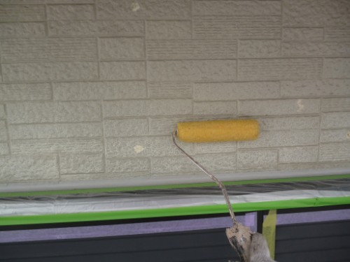 koushin_P1050870-1 | 外壁塗装は神奈川県横浜市の塗装職人 Yellow paint roller applying paint to a textured brick-pattern exterior wall with masking tape below.