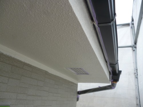 koushin_P1050873-1 | 外壁塗装は神奈川県横浜市の塗装職人 Low-angle view of a building’s soffit showing a small vent, a gutter/downspout, and scaffolding along the right side.