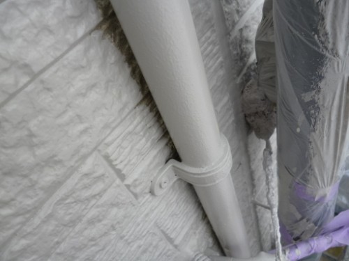 koushin_P1050883-1 | 外壁塗装は神奈川県横浜市の塗装職人 White conduit pipe strapped to a textured exterior wall with a circular clamp; protective wrap on the right edge shows possible construction work.