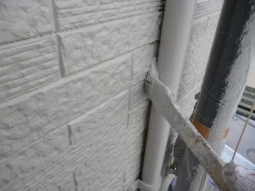 koushin_P1050884-1 | 外壁塗装は神奈川県横浜市の塗装職人 Close-up of a textured exterior wall with a white PVC pipe and taped joint, near scaffolding or temporary supports.