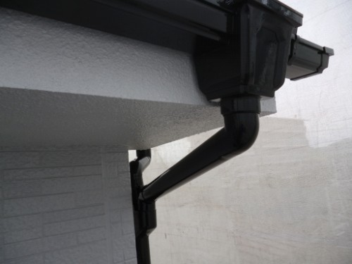 koushin_P1050890-1 | 外壁塗装は神奈川県横浜市の塗装職人 Close-up of a black plastic rain gutter and downspout connected to a white building exterior.