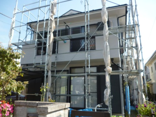 koushin_P1050892-1 | 外壁塗装は神奈川県横浜市の塗装職人 Two-story house under scaffolding during renovation, with metal frames surrounding the exterior and wrapped areas on the windows.
