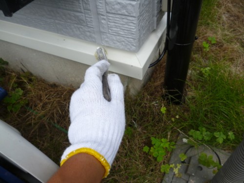 koushin_P1050904-1 | 外壁塗装は神奈川県横浜市の塗装職人 Gloved hand applying sealant along the base of a concrete house foundation outdoors.