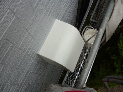 koushin_P1050906-1 | 外壁塗装は神奈川県横浜市の塗装職人 White rectangular exterior vent cover mounted on a gray brick wall, with a metal railing and hoses nearby.