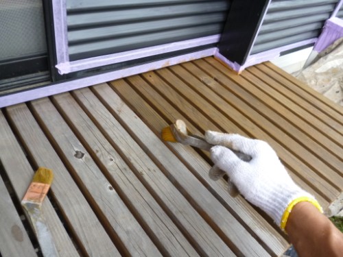 koushin_P1050909-1 | 外壁塗装は神奈川県横浜市の塗装職人 Gloved hand applying brown wood stain to outdoor deck boards with a brush in use on a sunny day.