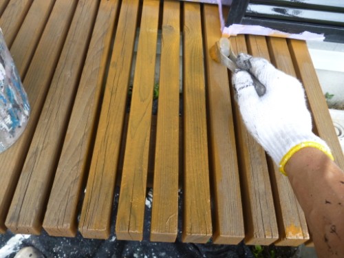 koushin_P1050913-1 | 外壁塗装は神奈川県横浜市の塗装職人 Close-up of a person wearing a white glove staining wooden slats of an outdoor bench with a brush.