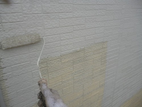 koushin_p1050874-1 | 外壁塗装は神奈川県横浜市の塗装職人 A hand in a glove paints a light beige patch on a textured white brick wall using a roller.