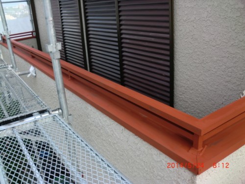Orange metal guardrail running along a beige stucco wall with black louvered vents and metal construction scaffolding nearby.