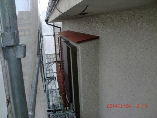 Narrow alley between buildings with metal scaffolding on the left, a beige stucco wall, and a small window with a red overhang. Timestamp in red at bottom right.