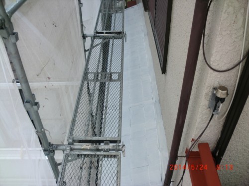 Metal scaffolding runs along the exterior of a building, viewed from a narrow work platform with guardrails.