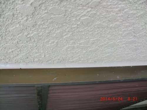 Textured beige stucco wall above a brown window frame with glass panels; a red timestamp appears in the bottom-right corner.