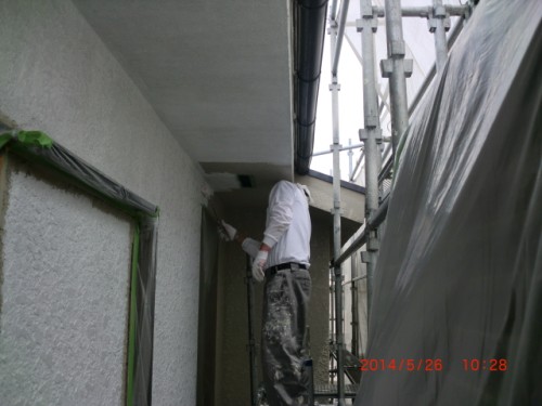 Construction worker on scaffolding painting the exterior wall; plastic sheeting covers the adjacent area.