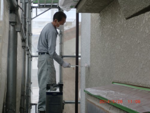 Construction worker on scaffolding wearing a mask and gloves, painting an exterior wall with a roller.
