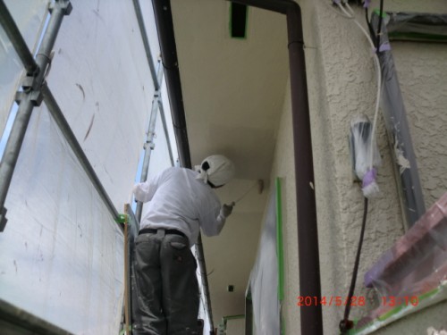 Construction worker in a white protective suit on scaffolding, applying plaster to a ceiling near a doorway under construction.