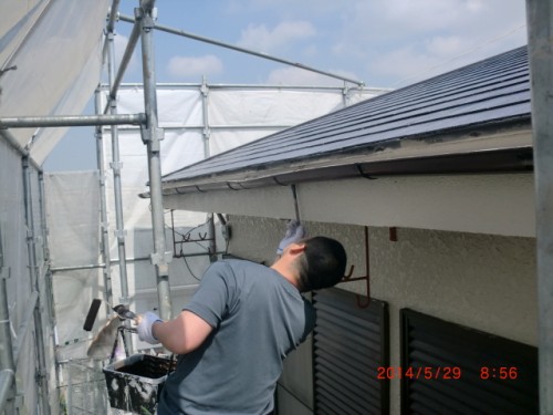 Worker on scaffolding painting the eaves of a house with a roller on a sunny day