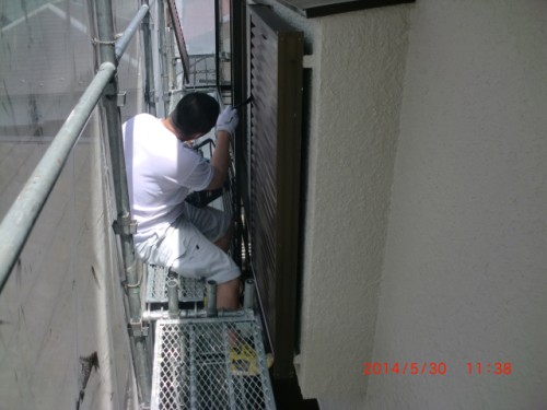 Maintenance worker on metal scaffold beside a building, repairing an exterior panel on the wall.