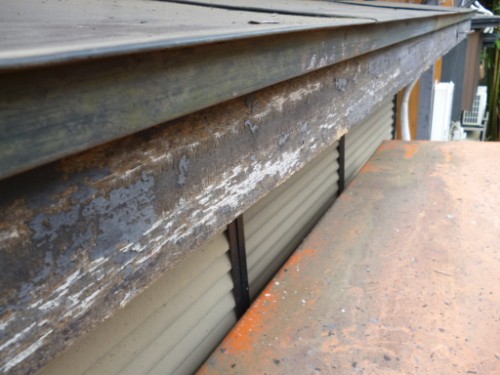 Close-up of a rusted, peeling metal roof edge with worn paint along a residential building edge.