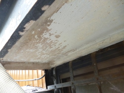 Rusty underside with peeling paint and exposed metal, showing corrosion along beams and pipes under a structure.