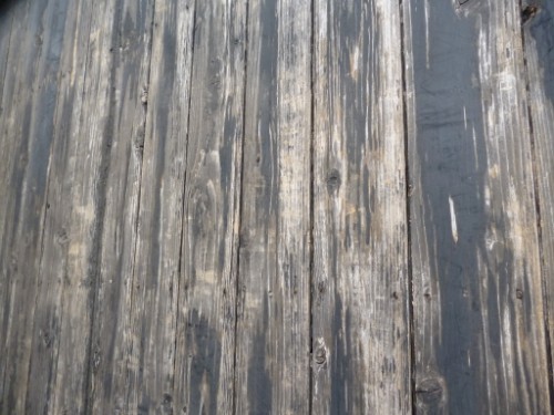 Close-up of weathered wooden deck boards with gray-brown tones and visible grain patterns.