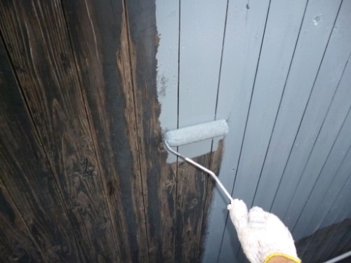 Close-up of a gloved hand using a paint roller to apply white paint to a wooden wall.