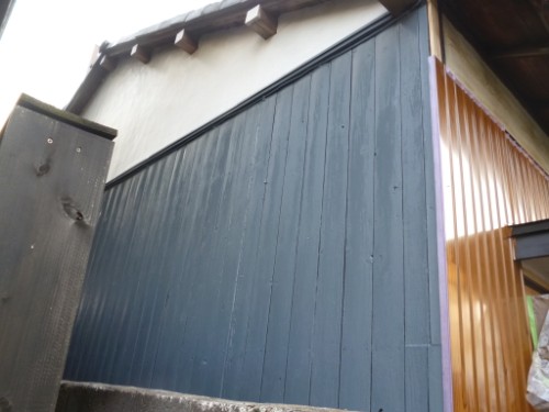 Blue vertical siding wall of an outdoor building with a sloped roof and a brown metal panel on the right; concrete steps at the base.